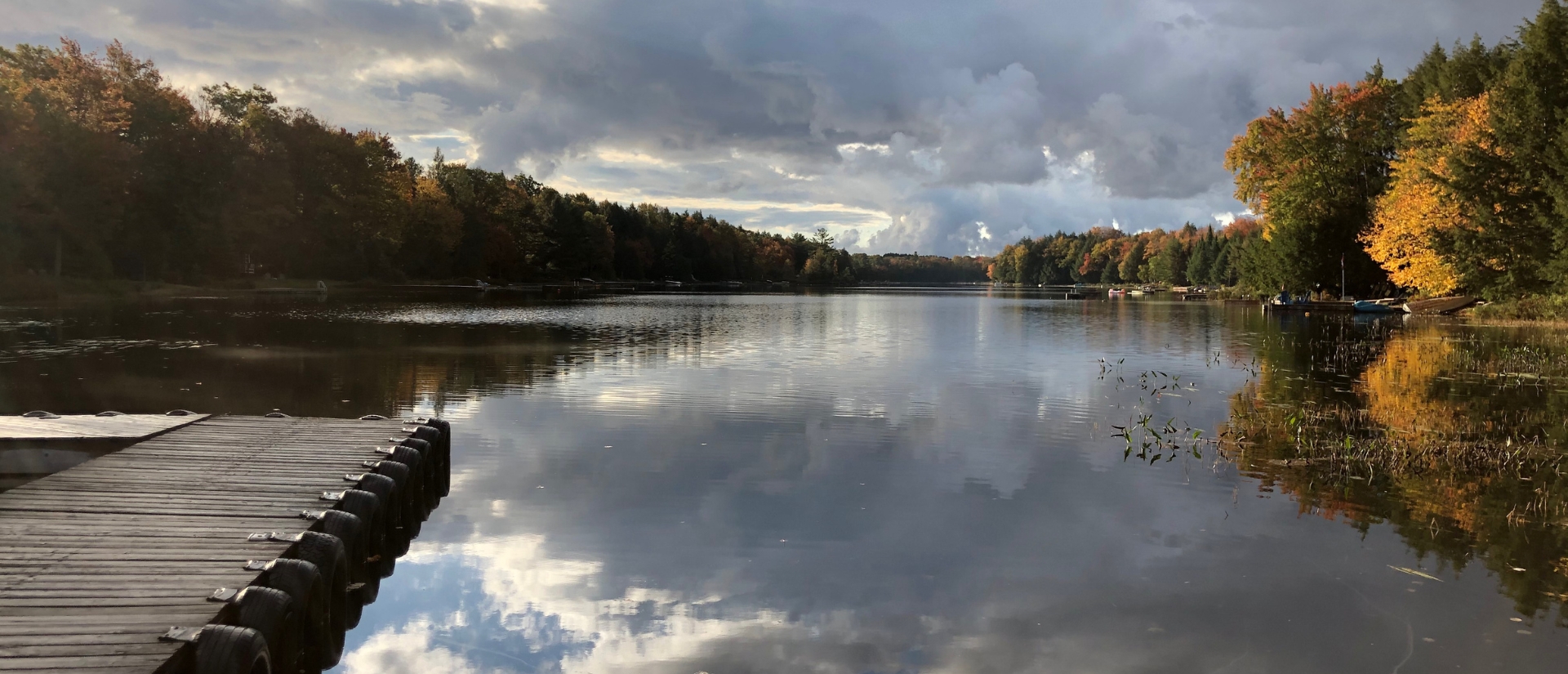 A dock extended out onto a clear lake with the sky reflecting off of it
