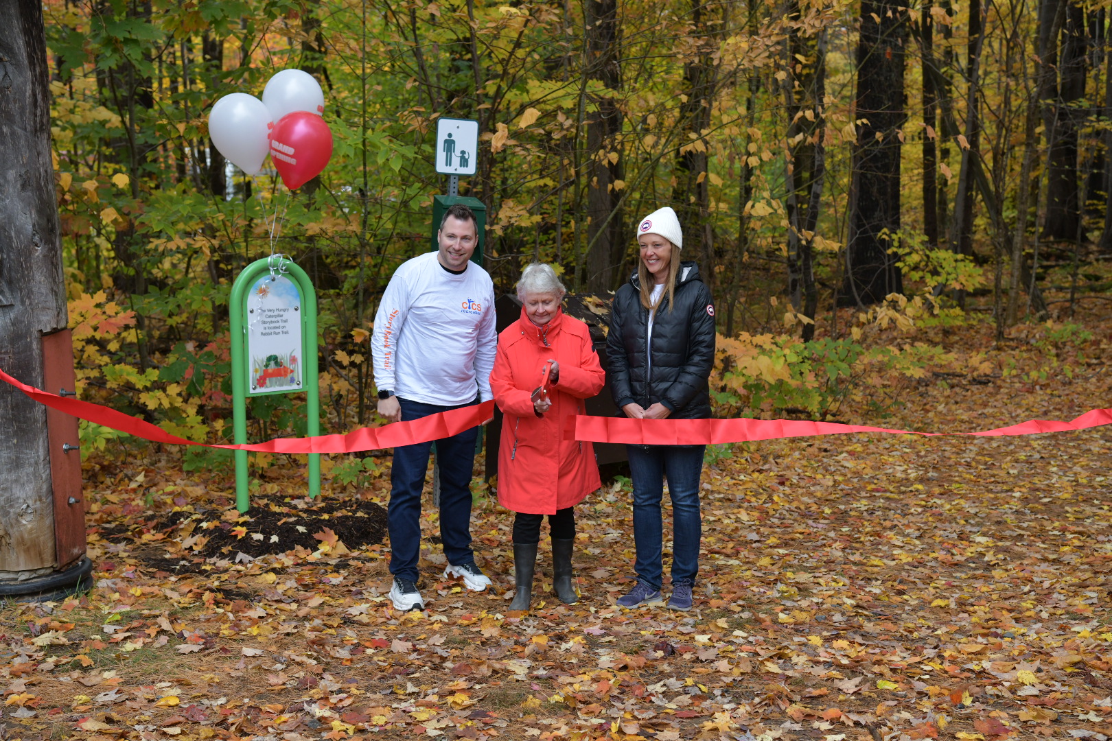 three people cutting a ribbon on a trail in the fall