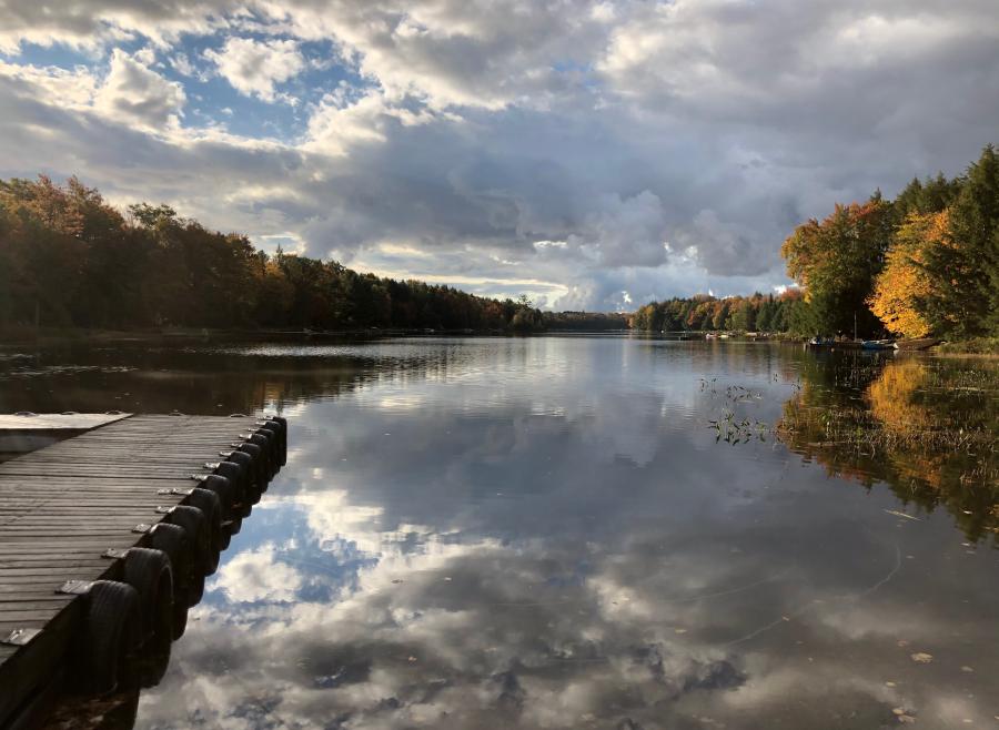 A dock extended out onto a clear lake with the sky reflecting off of it