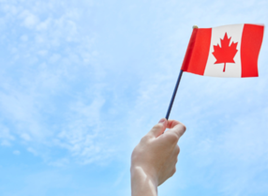 Canada flag in hand against blue sky