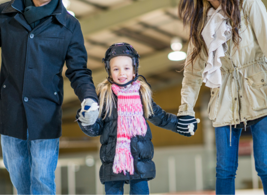 Adult male and adult female holding hand of girl in arena skating