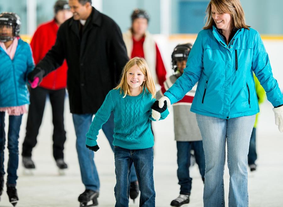 Multiple adults and children skating on an ice rink indoors