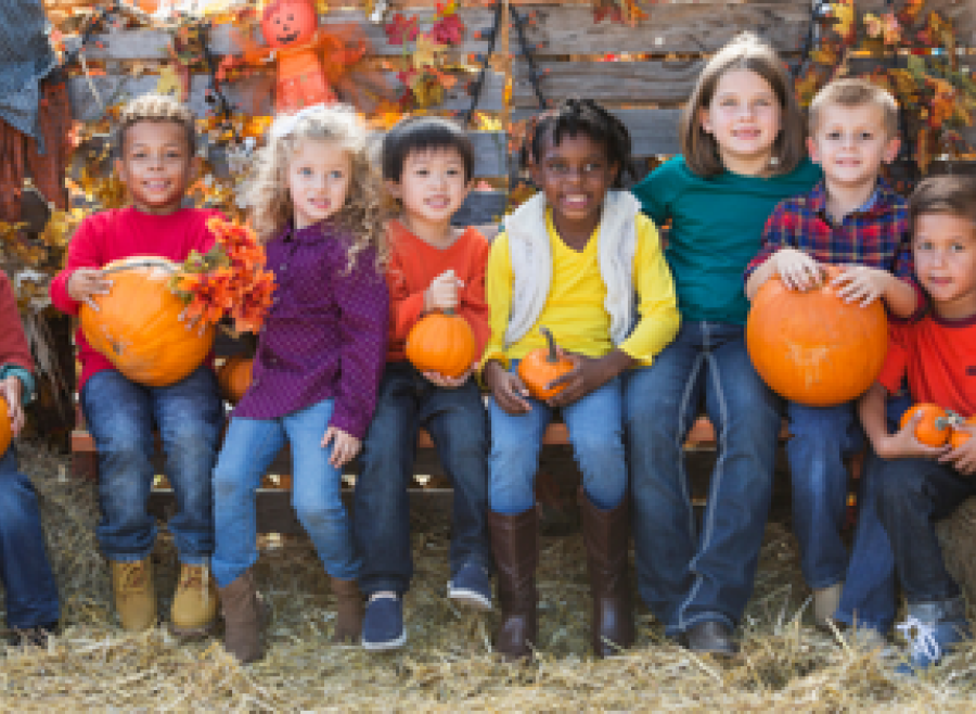 Children sitting on hay bales with pumpkins