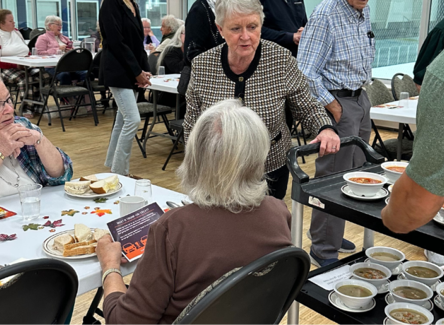 senior women seated at table being served soup by another senior woman