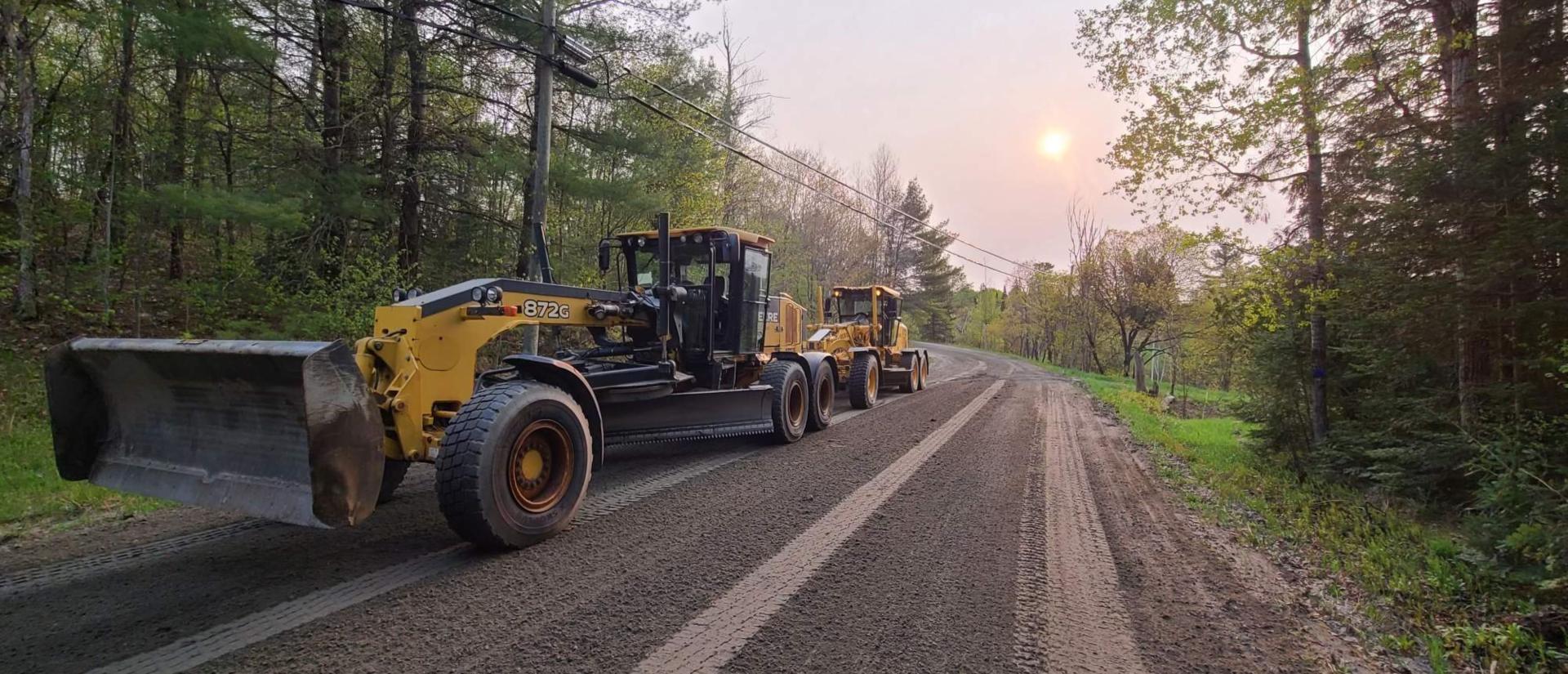A couple of graders on a forested dirt road in the early summer morning