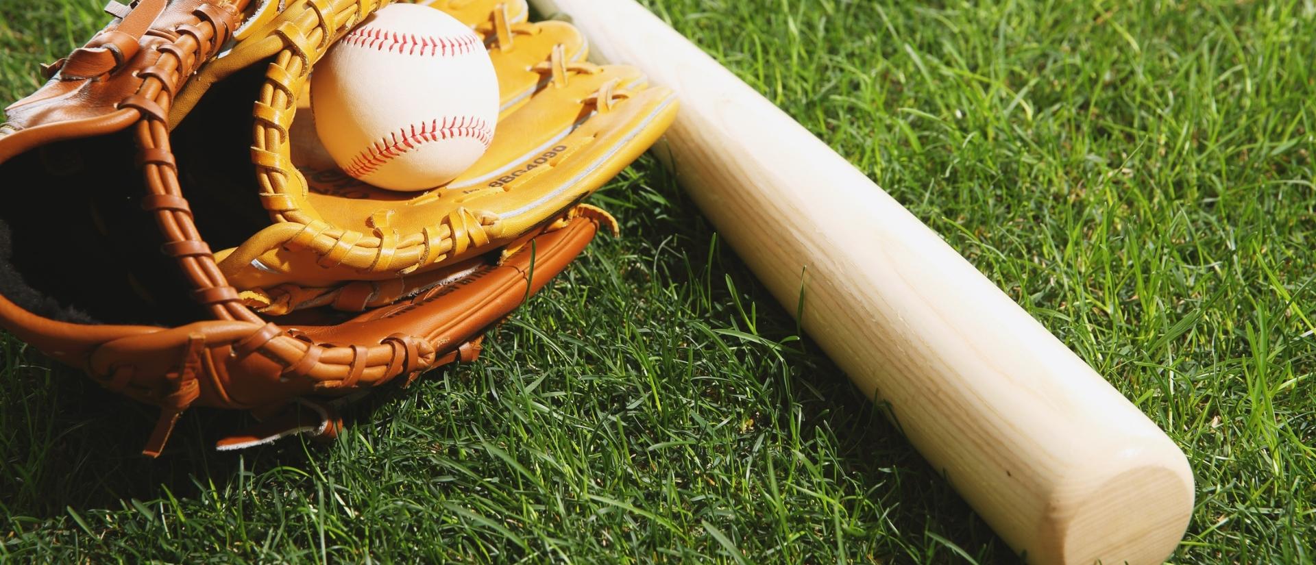 A baseball inside of a baseball glove lying next to a baseball bat on a grassy surface