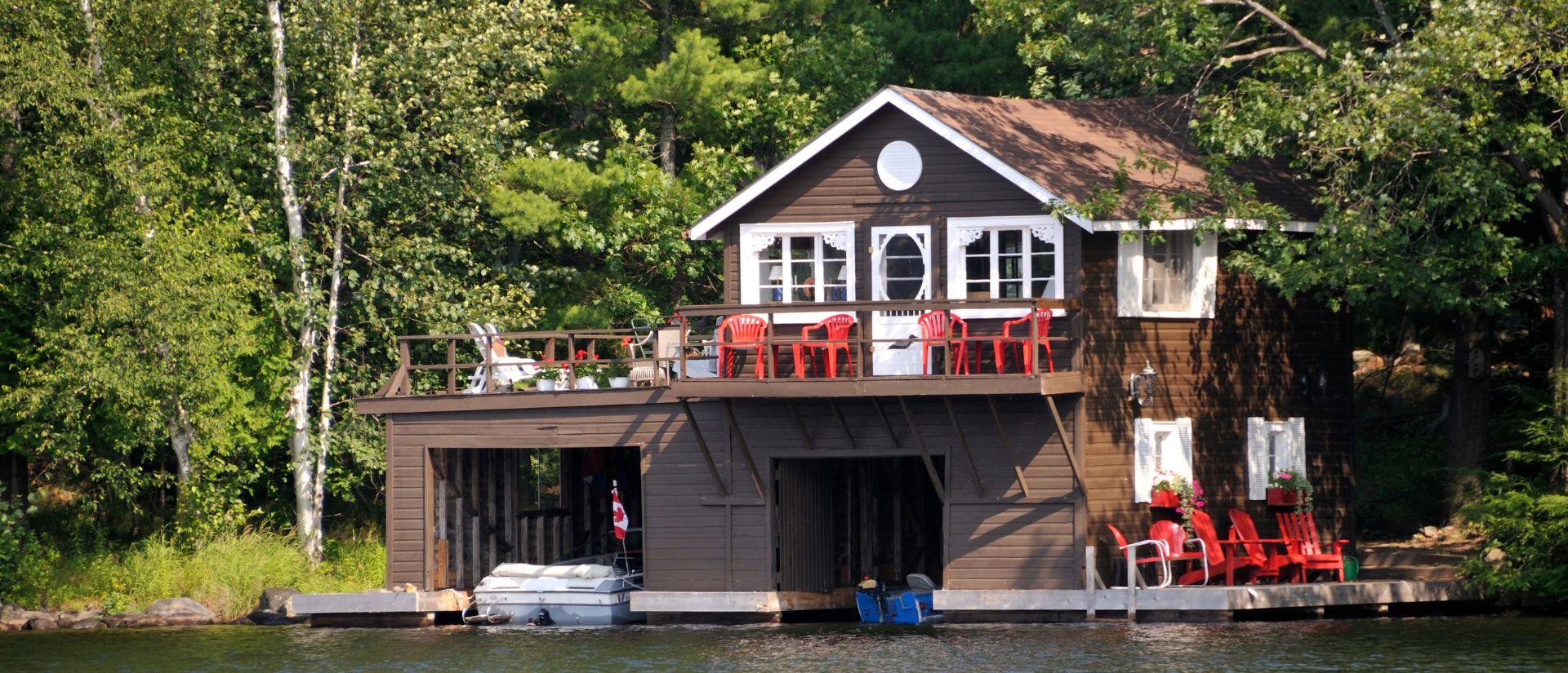 A charming lakeside boathouse surrounded by lush greenery, featuring a wooden deck adorned with bright red chairs, conveying a peaceful, rustic vibe.