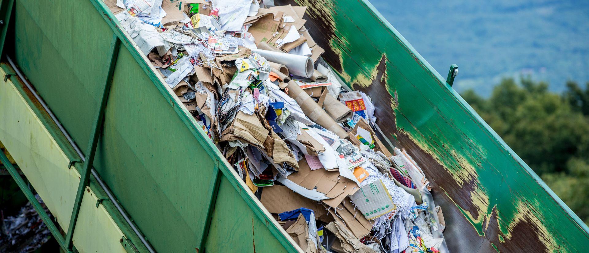 A green dumpster with crumpled cardboard and paper waste