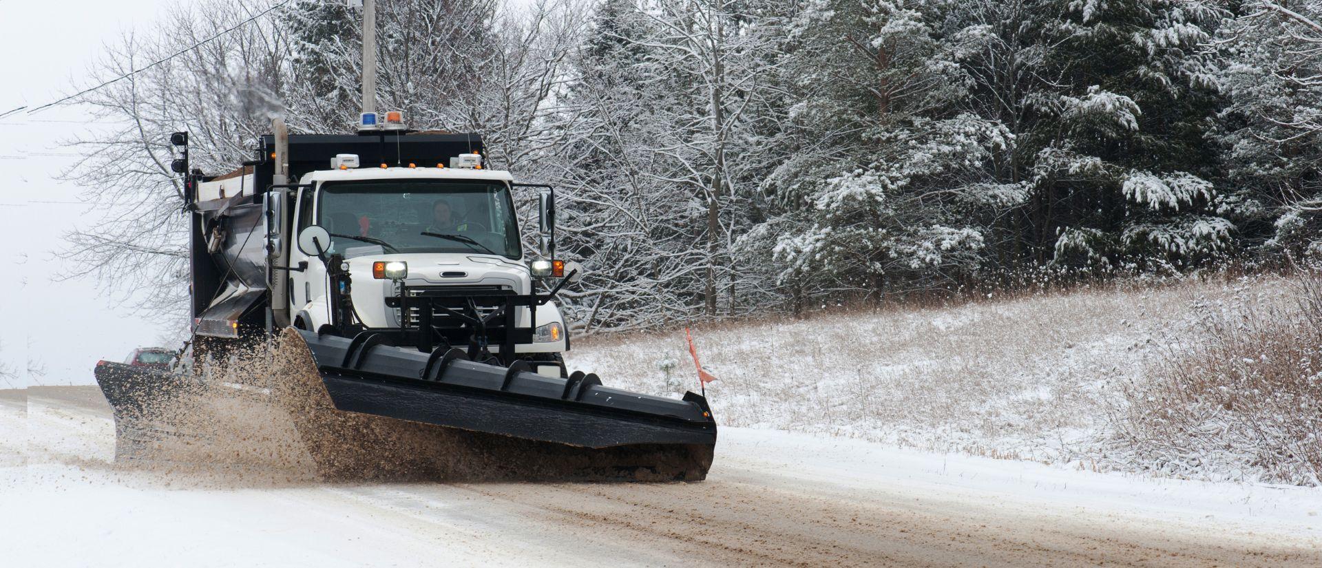 A snowplow plowing a snowy rural road