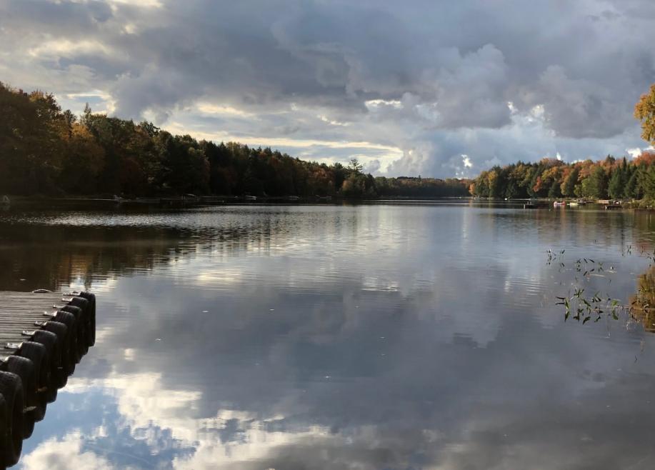 A dock extended out onto a clear lake with the sky reflecting off of it